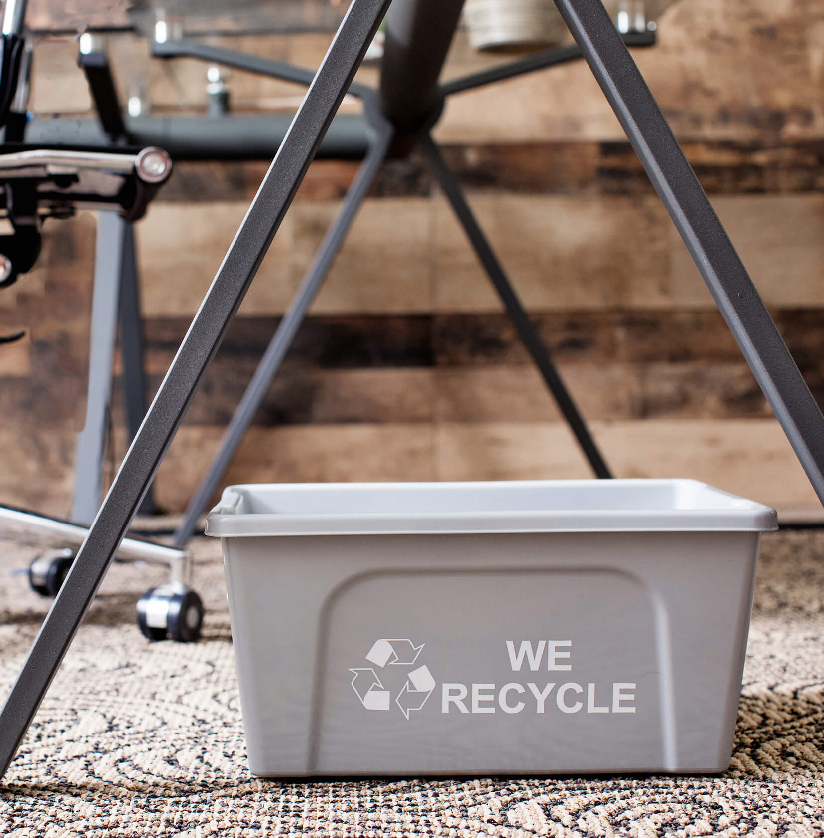 grey plastic deskside paper recycling container with we recycled printed on the side sitting on the floor in an office