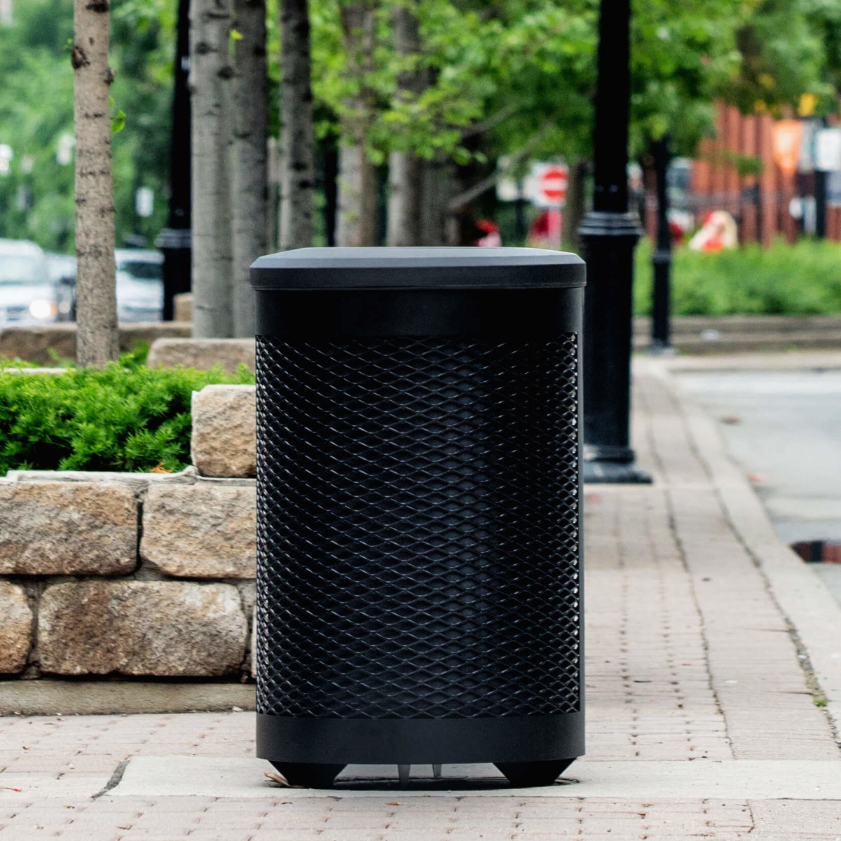 black powder coated steel waste container with a black plastic lid and liner on the side of a busy city street