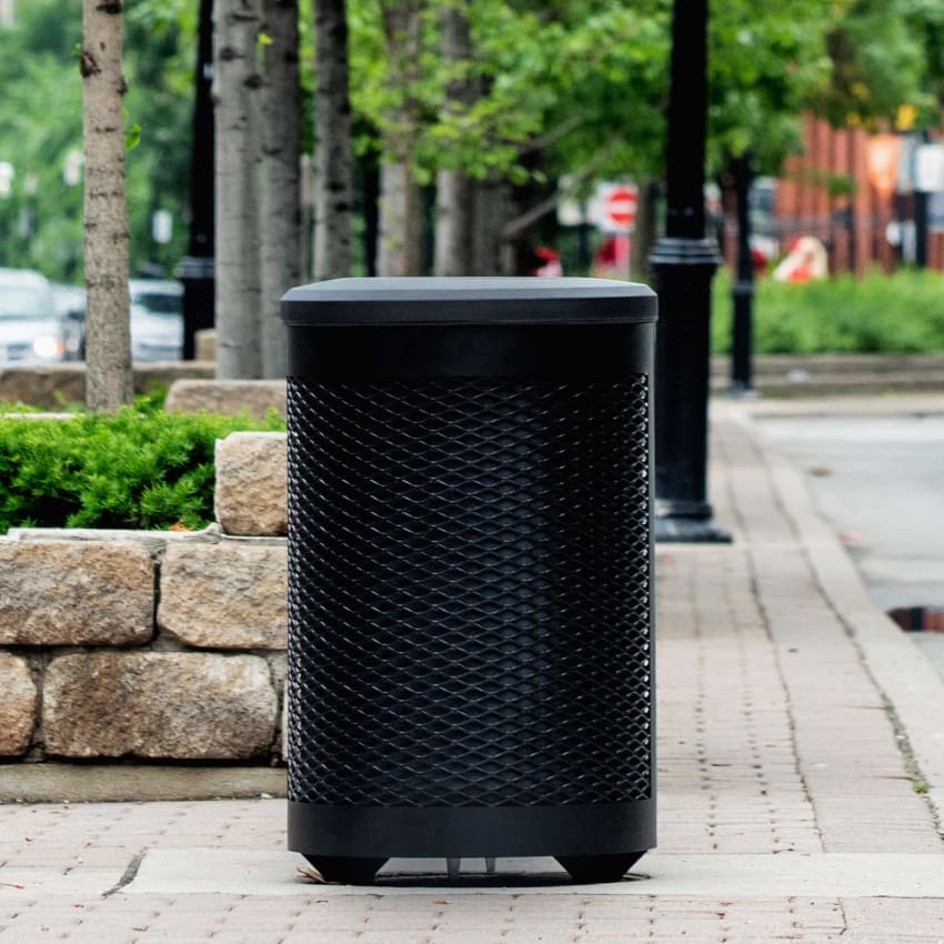 black powder coated steel waste container with a black plastic lid and liner on the side of a busy city street