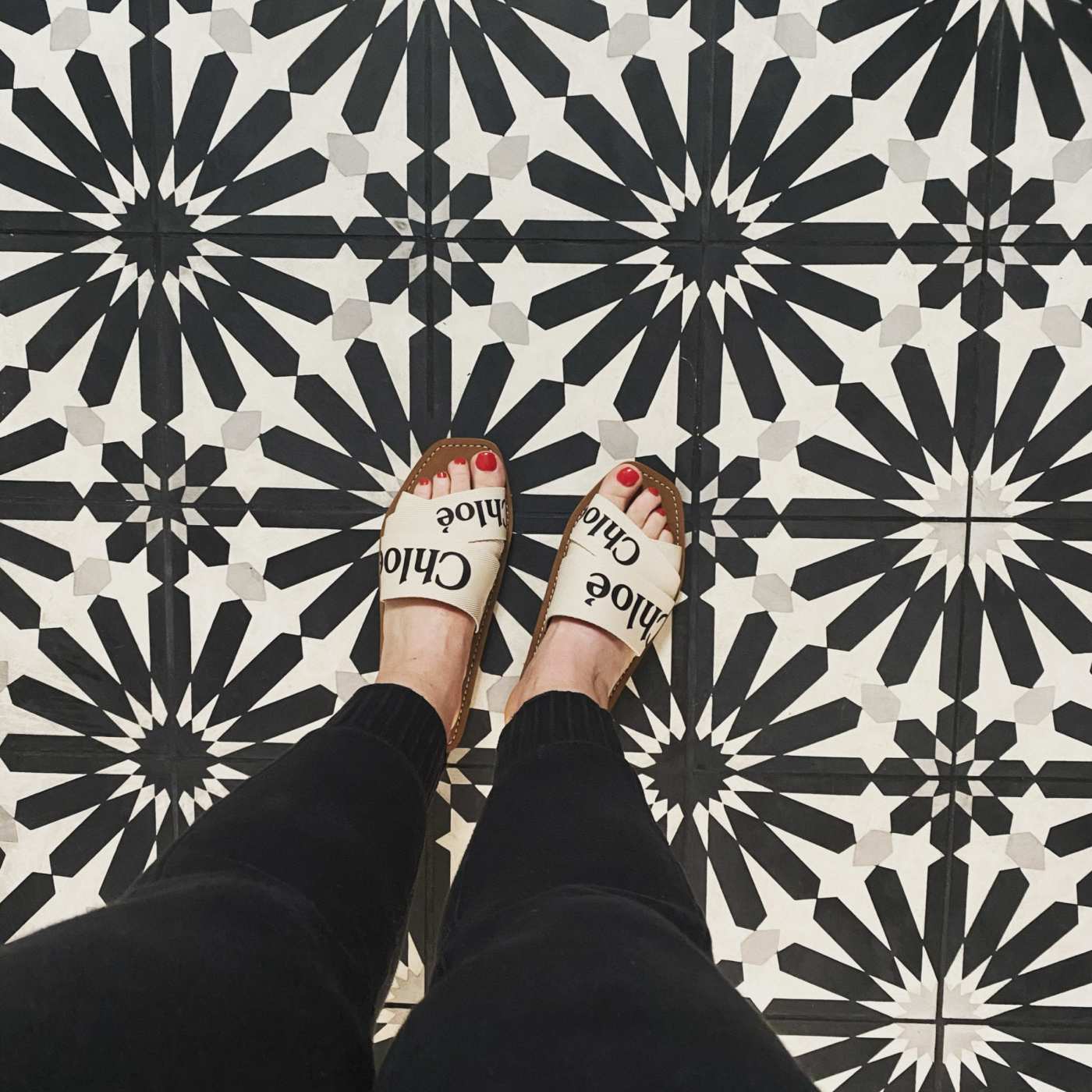 a person's feet standing on a black and white tile floor.