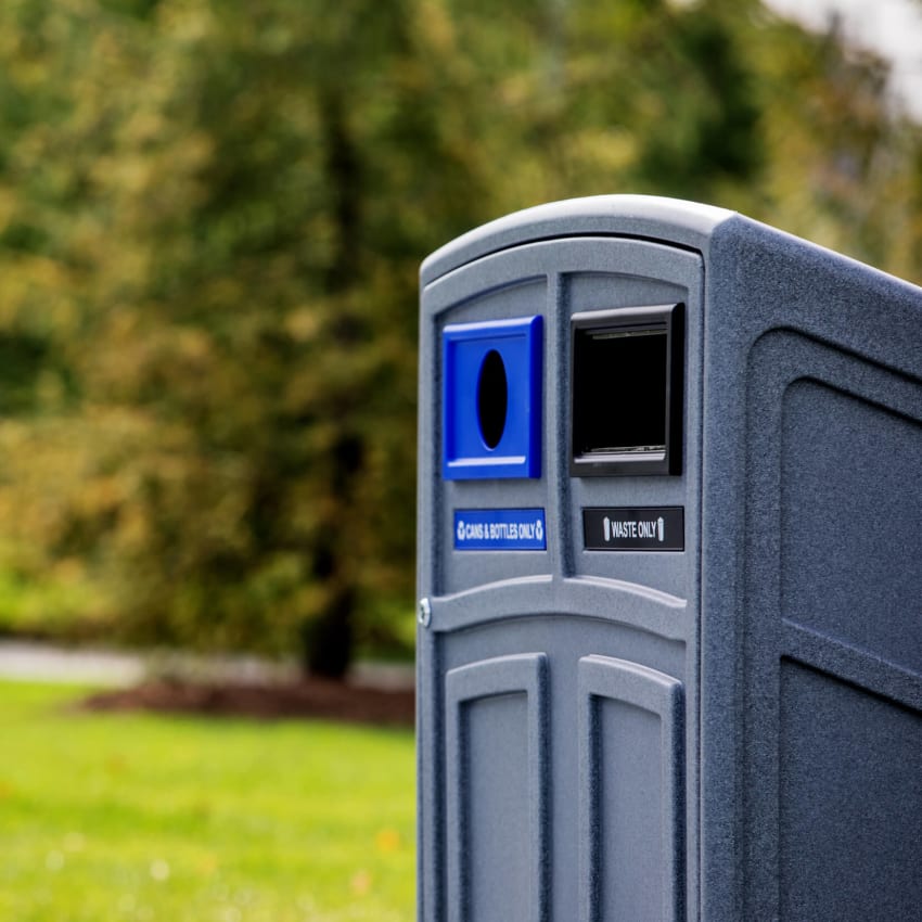 closeup of a grey plastic trash and recycling bin with color-coded restrictive openings and labels at an outdoor park
