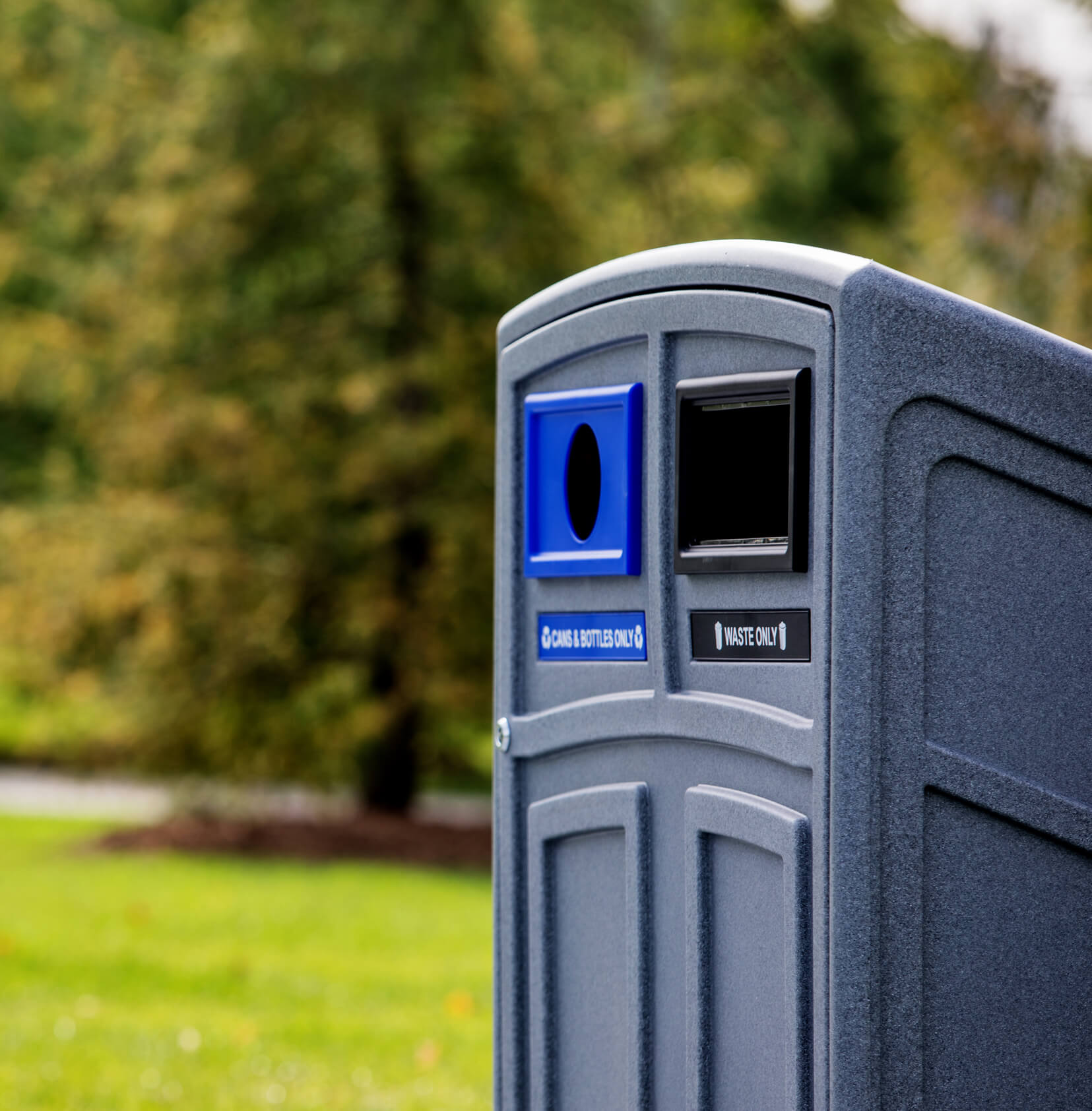 closeup of a grey plastic trash and recycling bin with color-coded restrictive openings and labels at an outdoor park