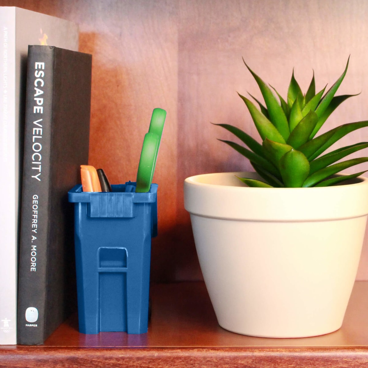 mini blue recycling cart on a bookshelf sitting beside a plant with pens and scissors inside