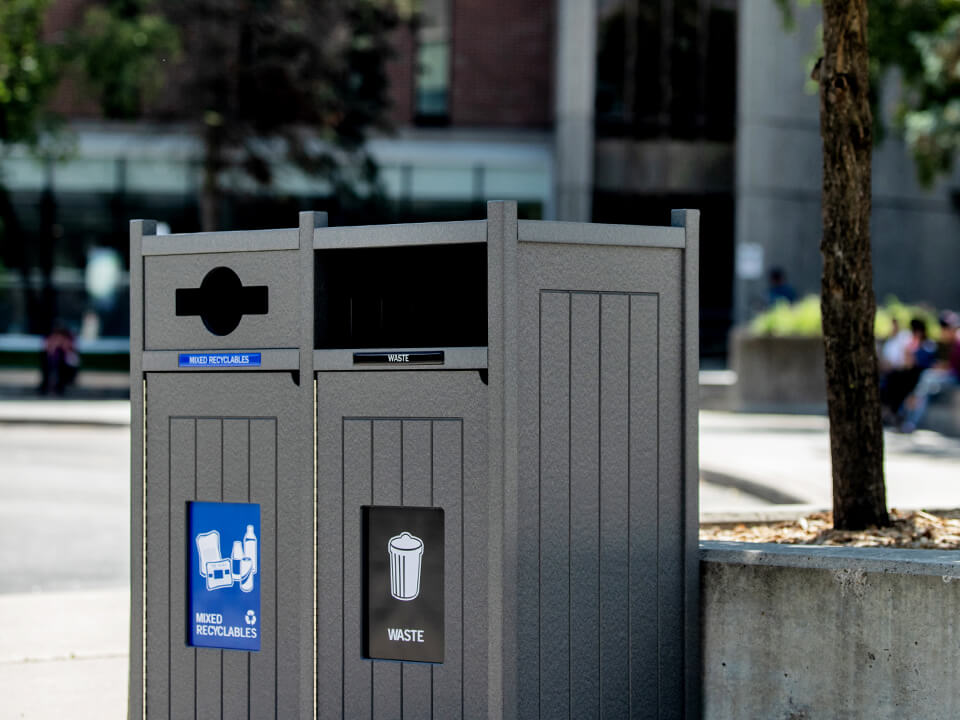 grey double recycling and trash bin with signs and labels outdoors at a busy college campus