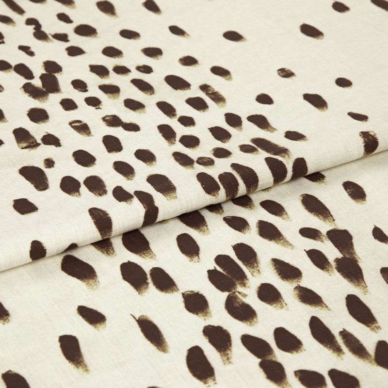Beige woven fabric with irregular dark-brown brushstroke spots, folded once with a visible overlap; close-up studio view showing texture and soft, even lighting on a neutral background.