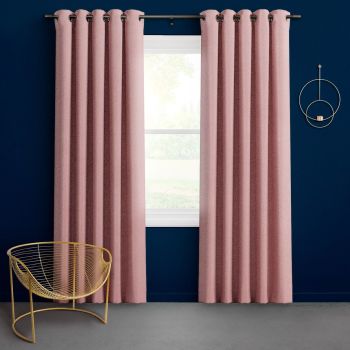 Textured pink grommet-top floor-length curtains hang slightly parted on a metal rod, framing daylight from a single-pane window in a navy-walled room with a gold wire chair and circular sconce.