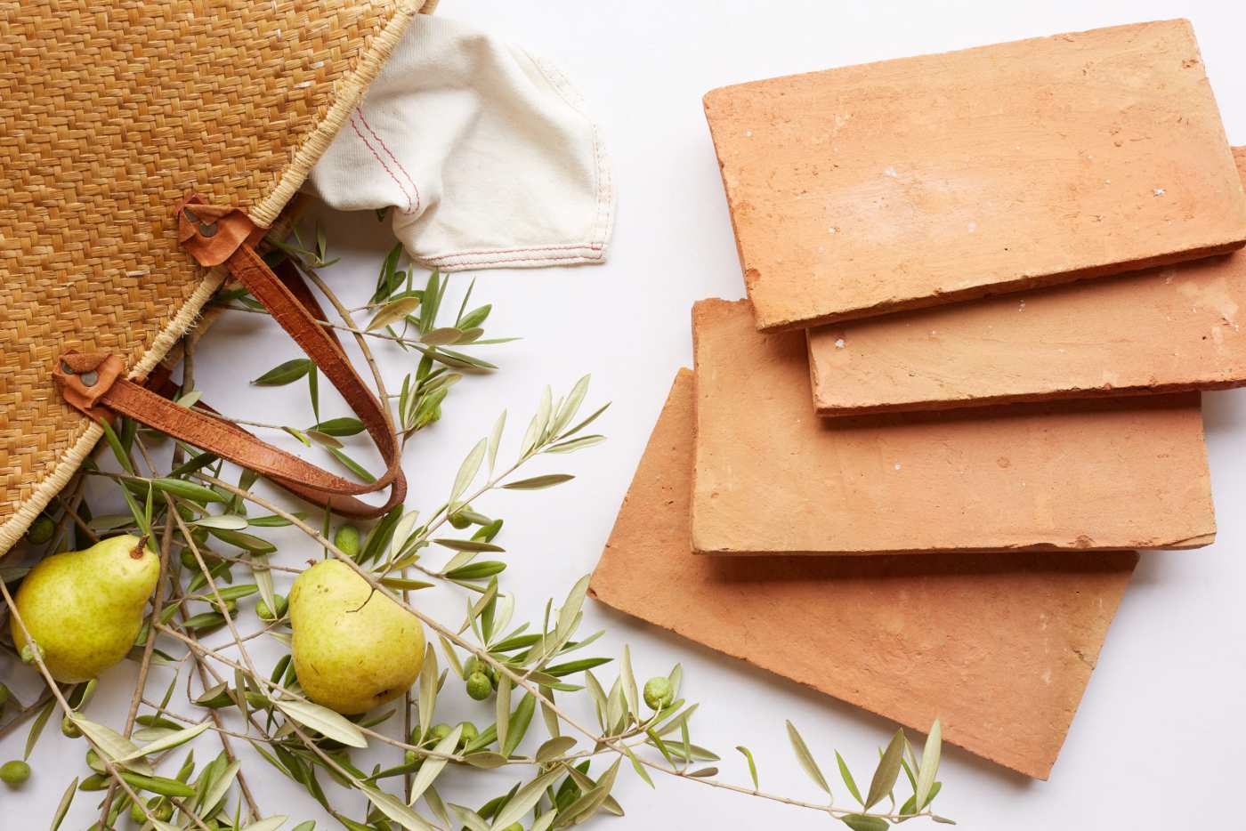 a stack of red rectangle tiles, a bag, some leaves, and two pears on a white surface.