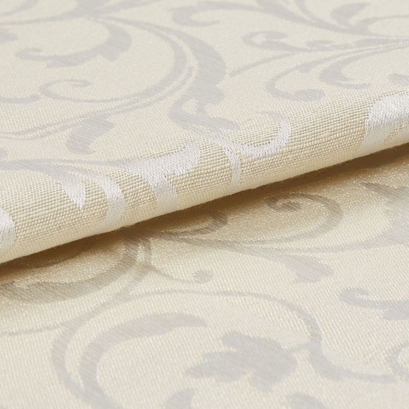 Cream damask curtain fabric swatch, folded with raised woven scroll motifs, reflecting subtle sheen; close-up macro view showing textured weave and soft studio lighting on a neutral surface.