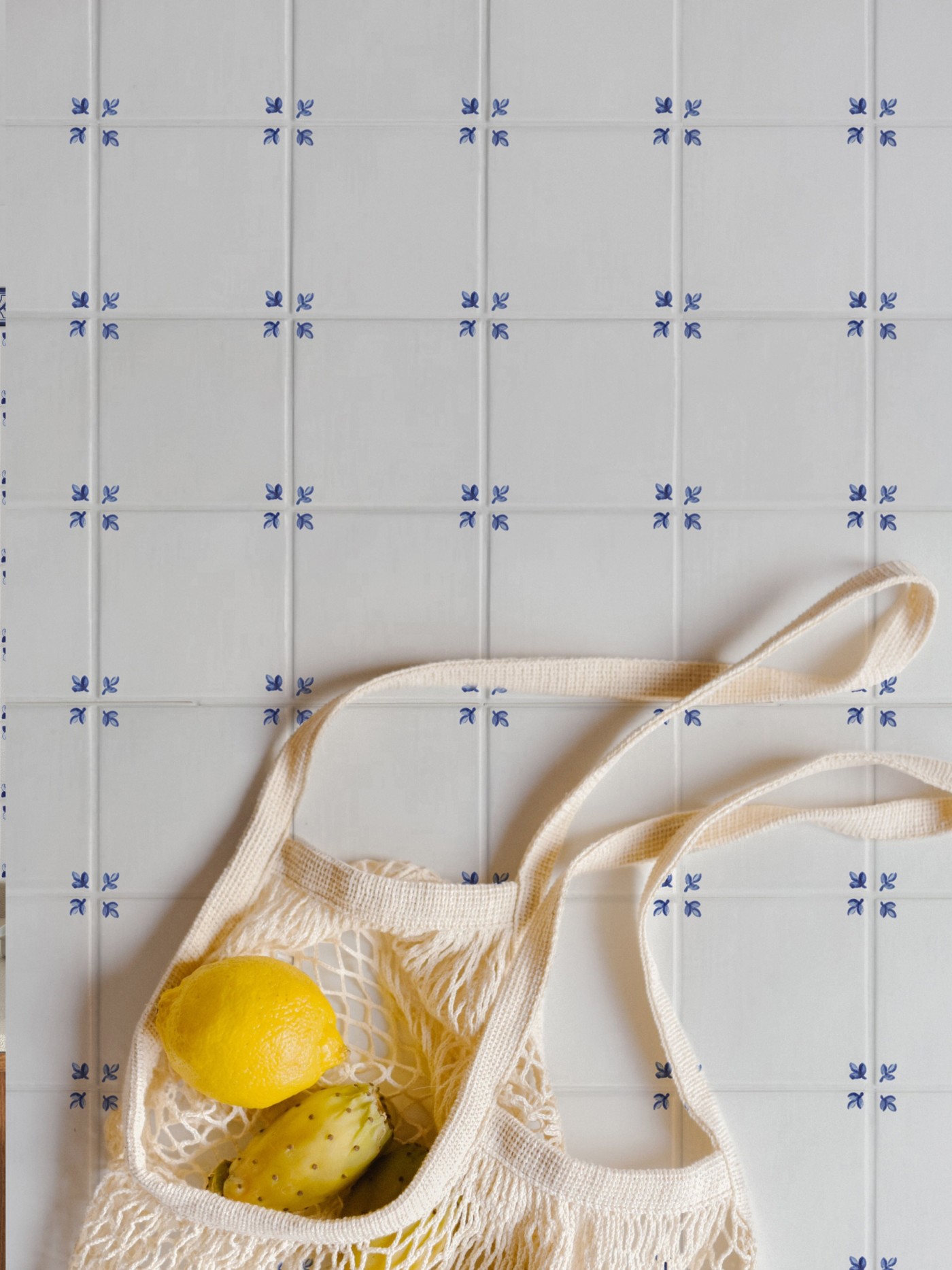 a shopping bag with lemons on top of a blue and white tiled floor.