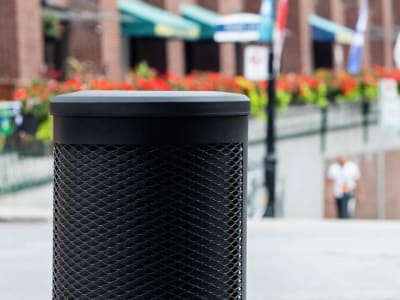 all black waste container with metal body and plastic lid perfect for keeping contents dry sitting beside an outdoor downtown restaurant patio