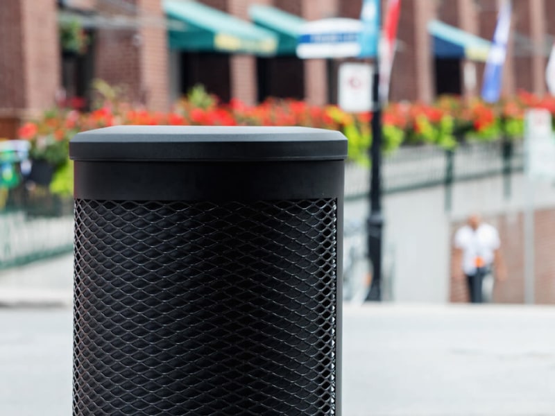 all black waste container with metal body and plastic lid perfect for keeping contents dry sitting beside an outdoor downtown restaurant patio