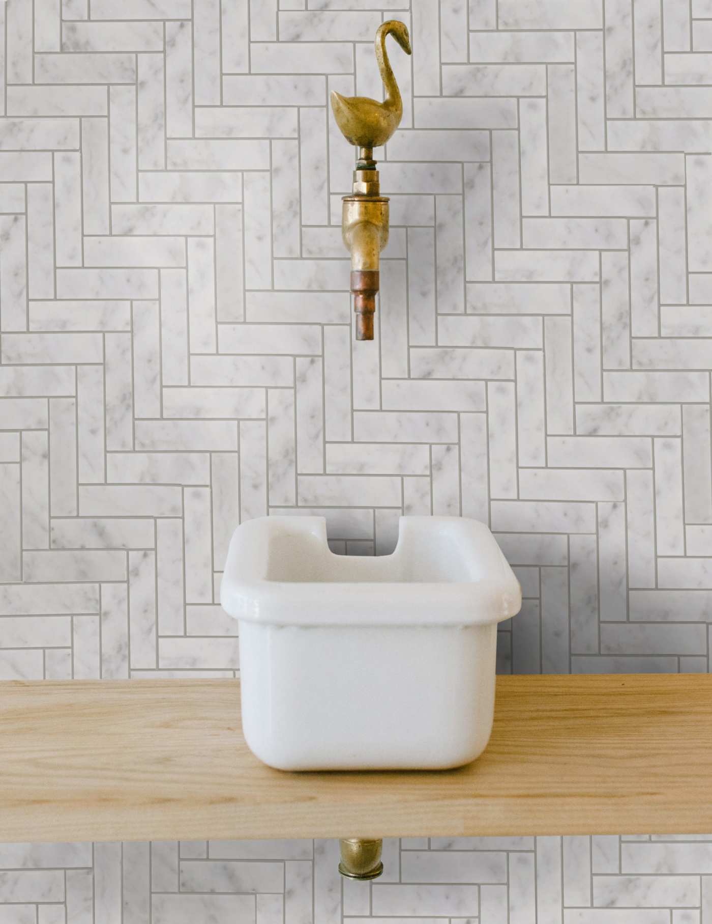 a white sink with a brass swan on top of the faucet.