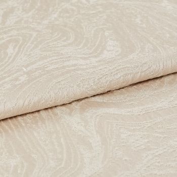 Beige jacquard fabric with subtle swirling embossed pattern, folded over itself; close-up view showing raised texture and soft sheen, neutral lighting on a plain surface.