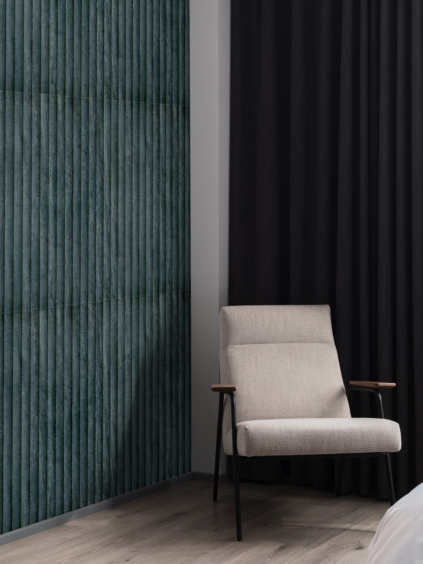 a room with a chair and a vertical green tile wall.