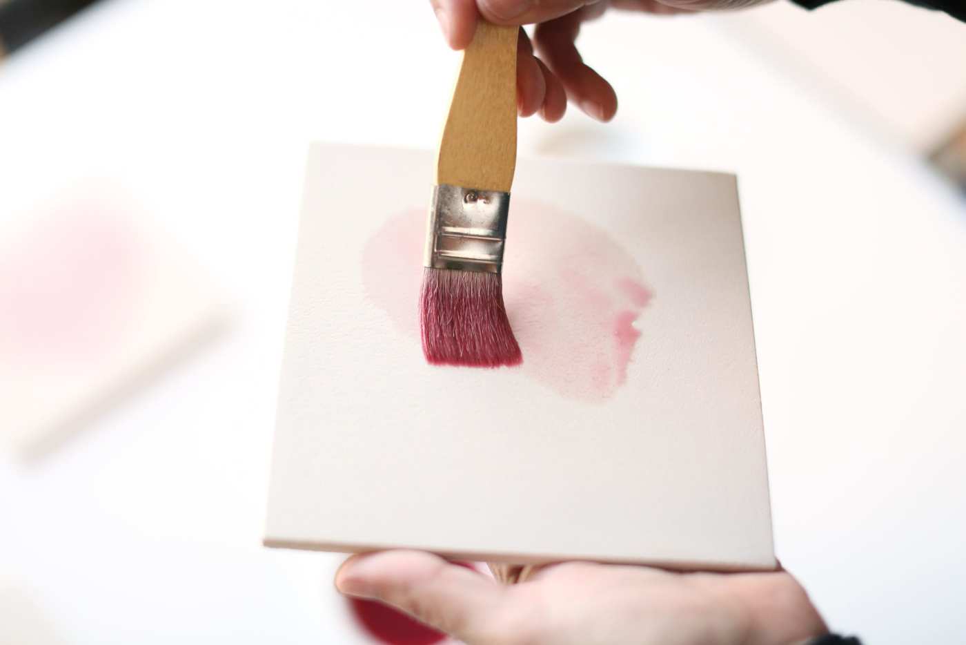 a person painting with a brush on a white tile.