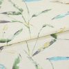 Linen-like curtain fabric, folded with a horizontal crease, printed with watercolor-style green, blue and yellow leaves; close-up studio shot on neutral beige background under soft light.