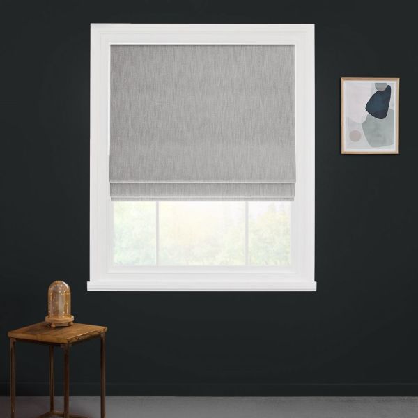 Light-gray Roman shade with soft horizontal folds, lowered and filtering daylight. White-trimmed window set in dark charcoal wall; small wooden side table with glass dome and framed abstract print nearby.