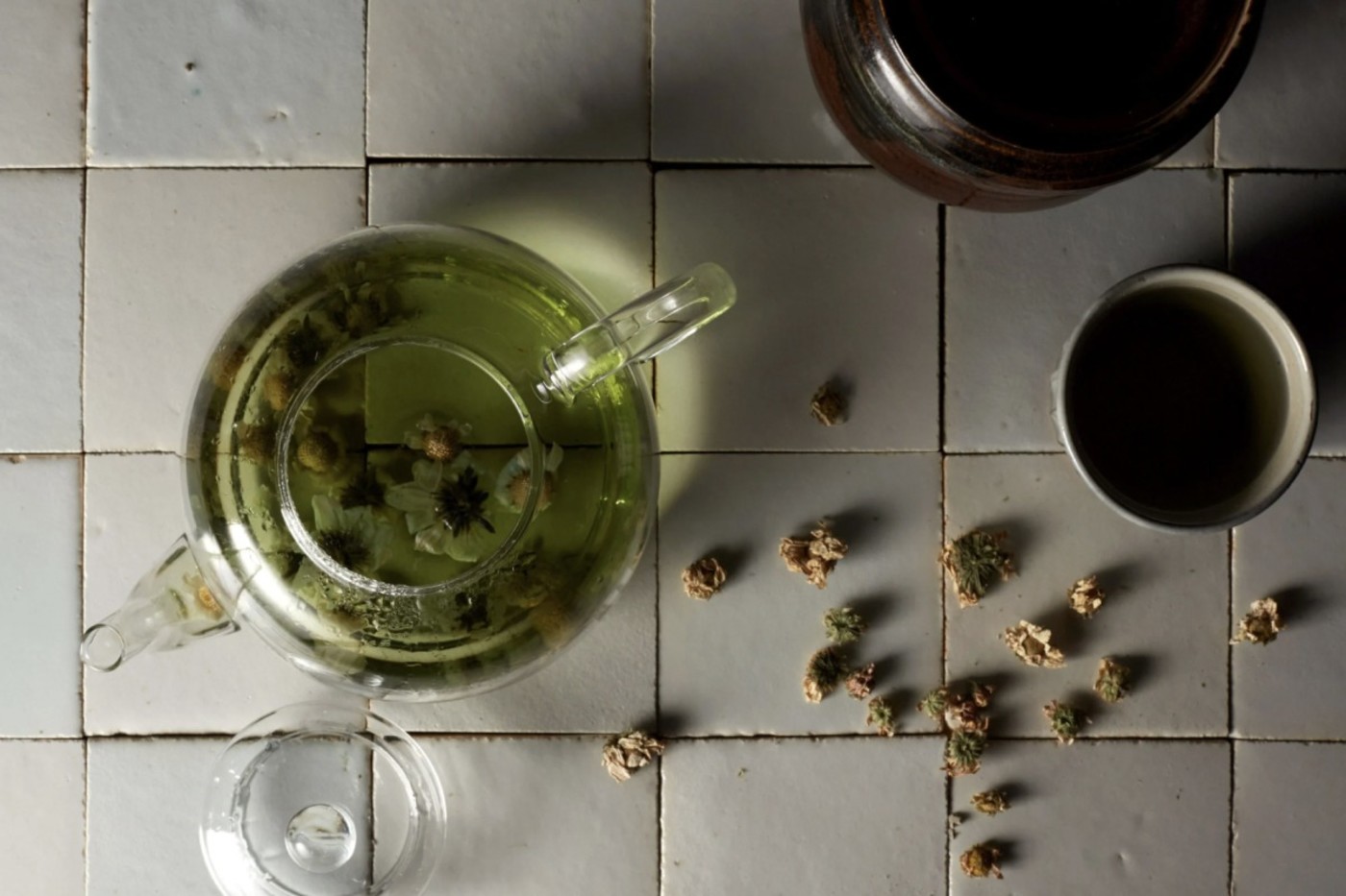 some dry flower buds and glass cups on a tiled surface.