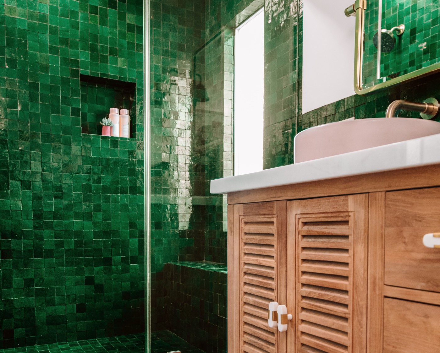 a bathroom with a green tiled shower and a wooden vanity.