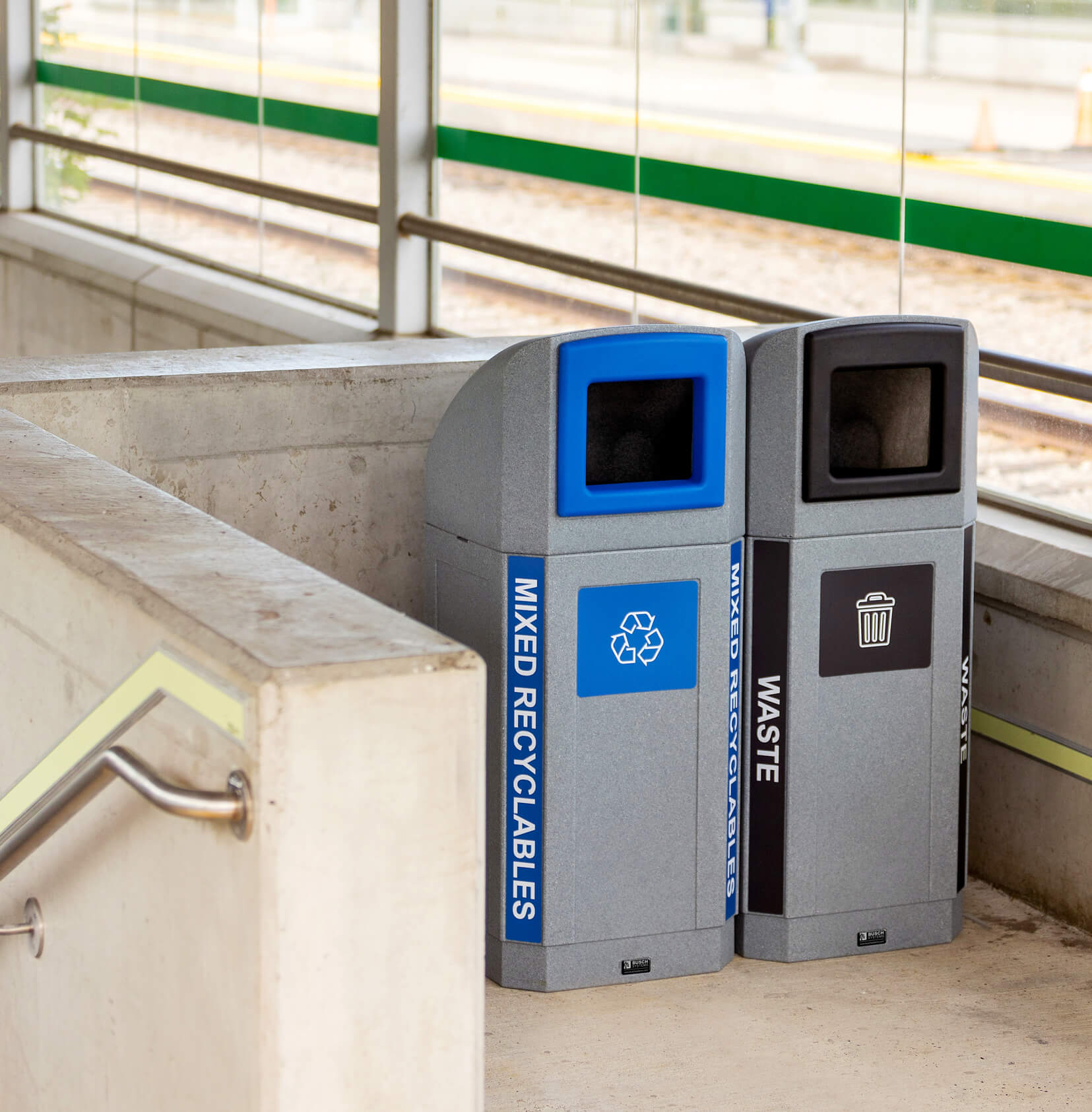 waste and mixed recyclables bins with canopy lids and color coded labelling at a train station