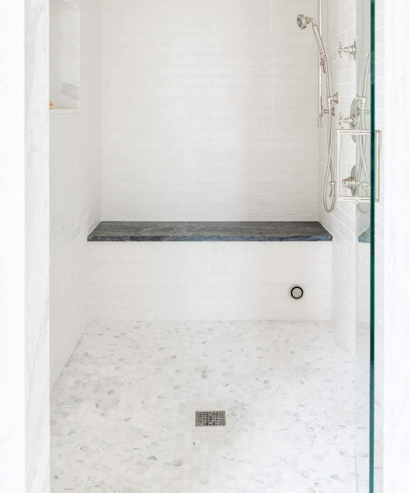 a white shower with a glass door and bench.