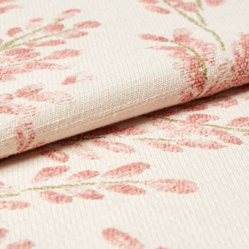 Cream woven fabric with raised pink floral embroidery, folded over along a seam; tufted stitches form leaf clusters. Close-up view of textured textile under soft, neutral lighting.