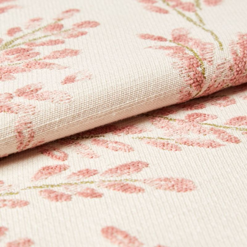 Cream woven fabric with raised pink floral embroidery, folded over along a seam; tufted stitches form leaf clusters. Close-up view of textured textile under soft, neutral lighting.