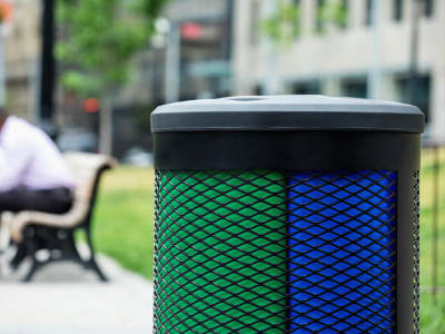 closeup of a triple stream waste and recycling collection bin with a black metal body and black plastic lid in a city park area