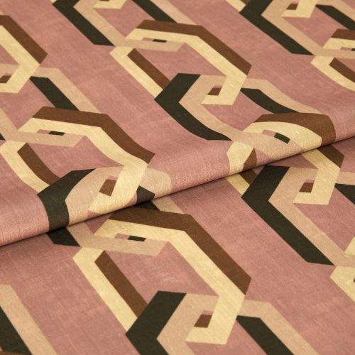 Geometric-patterned fabric with interlocking beige, brown and black hexagonal chains on a dusty rose background, folded across the center, lying on a flat surface under soft, neutral indoor lighting.