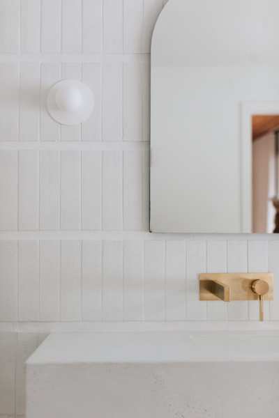 a white bathroom with a gold faucet and mirror.