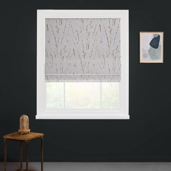 Patterned Roman blind lowered, filtering soft daylight through a white-framed window on a dark-gray wall; wooden side table with glass-dome lamp left, abstract art right, and blurred greenery beyond.