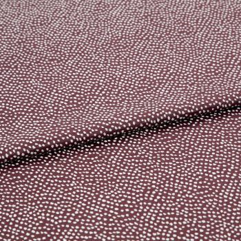 Burgundy fabric patterned with dense, irregular white dots, folded across the center; lying flat in a close-up studio shot, even lighting highlights its texture and subtle sheen.