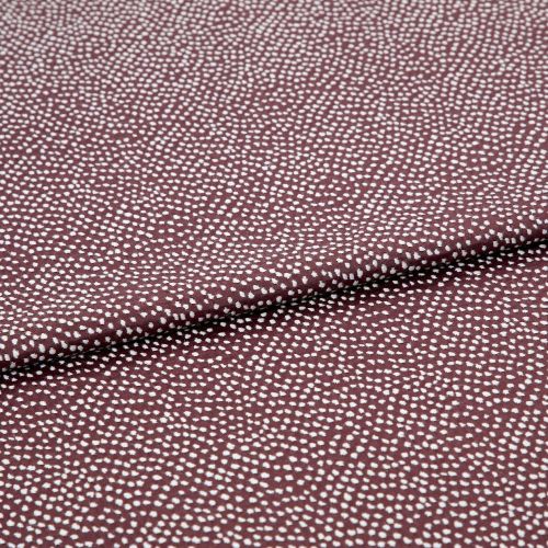 Burgundy fabric patterned with dense, irregular white dots, folded across the center; lying flat in a close-up studio shot, even lighting highlights its texture and subtle sheen.