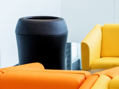 stylish all black plastic trash bin with large full opening lid placed at a college campus sitting area