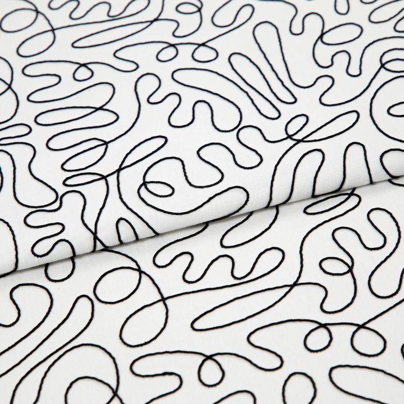White cotton fabric with continuous black embroidered squiggle pattern, folded once and overlapping; resting flat, showing stitched loops and curves under even studio lighting as a close-up textile sample.