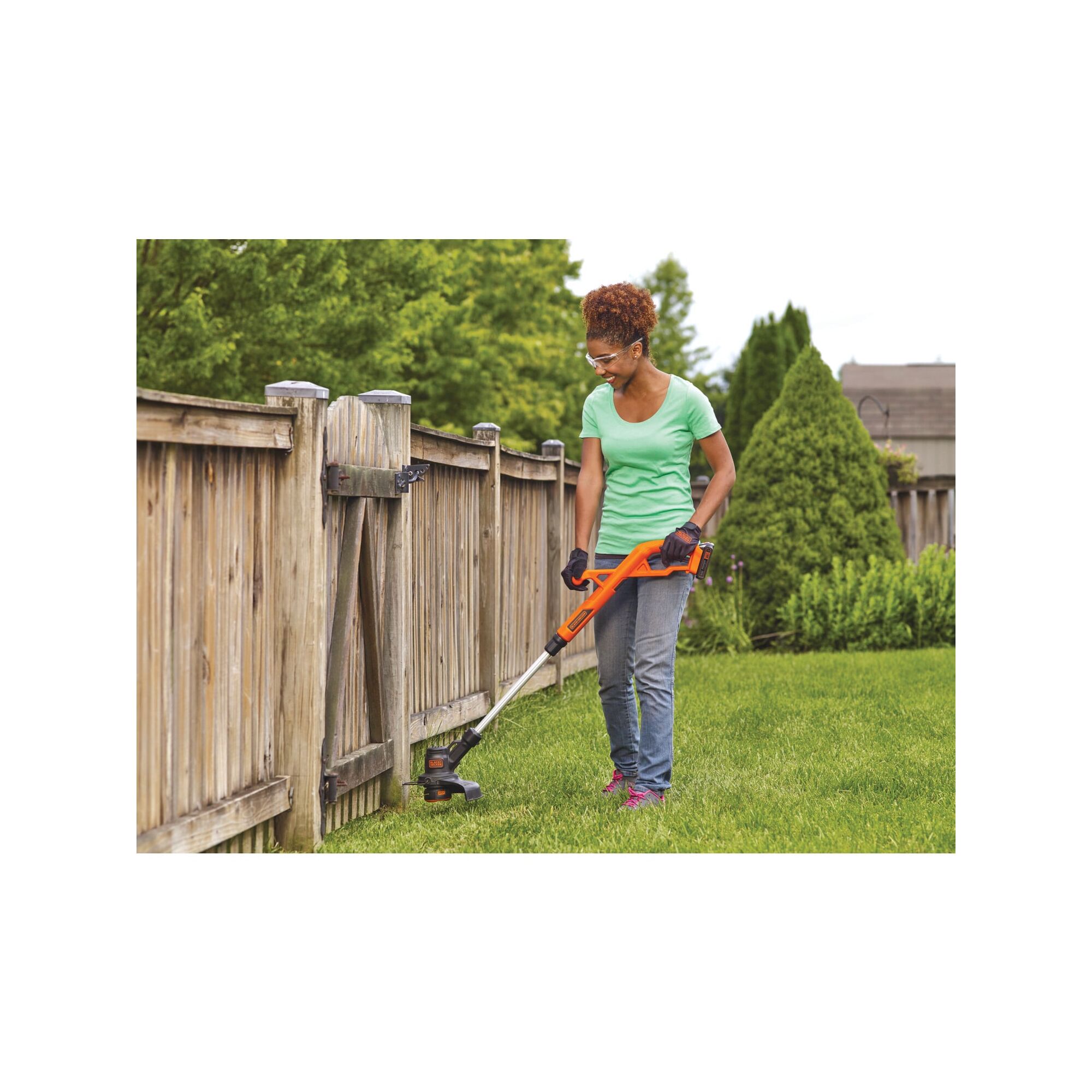 Woman using string trimmer near a wooden fence