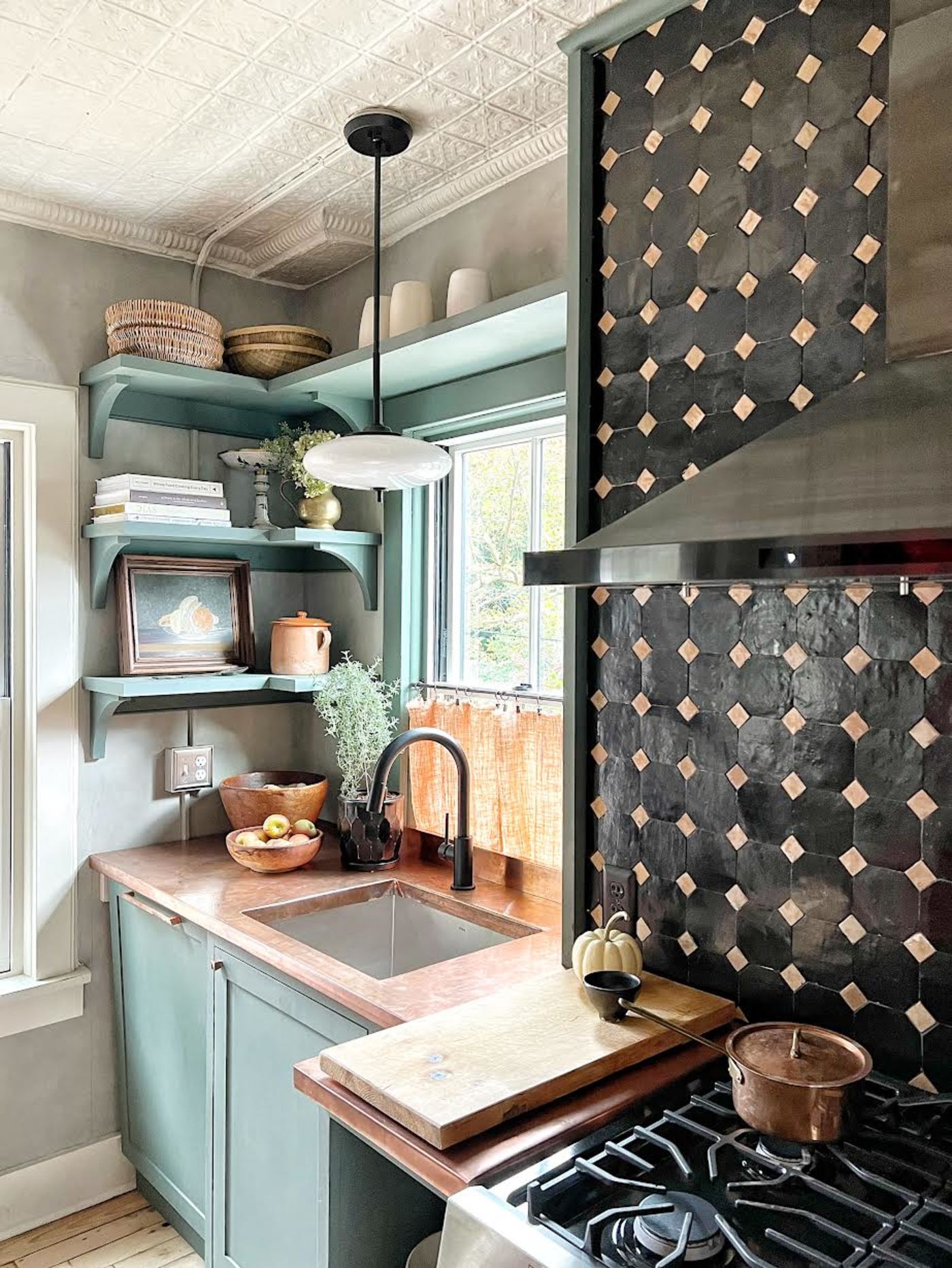 a kitchen with a stove, a sink and black and gold tiled backsplash.