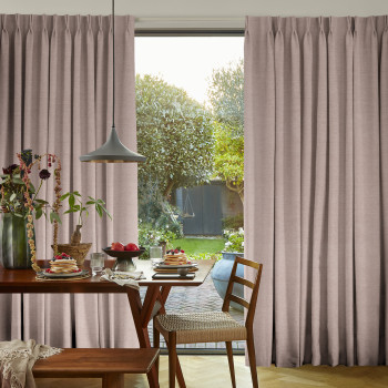 Beige pinch-pleat floor-to-ceiling curtains, parted centrally, framing and filtering soft daylight through a glass sliding door; a dining table set for breakfast and chairs in a sunlit, garden-facing room.