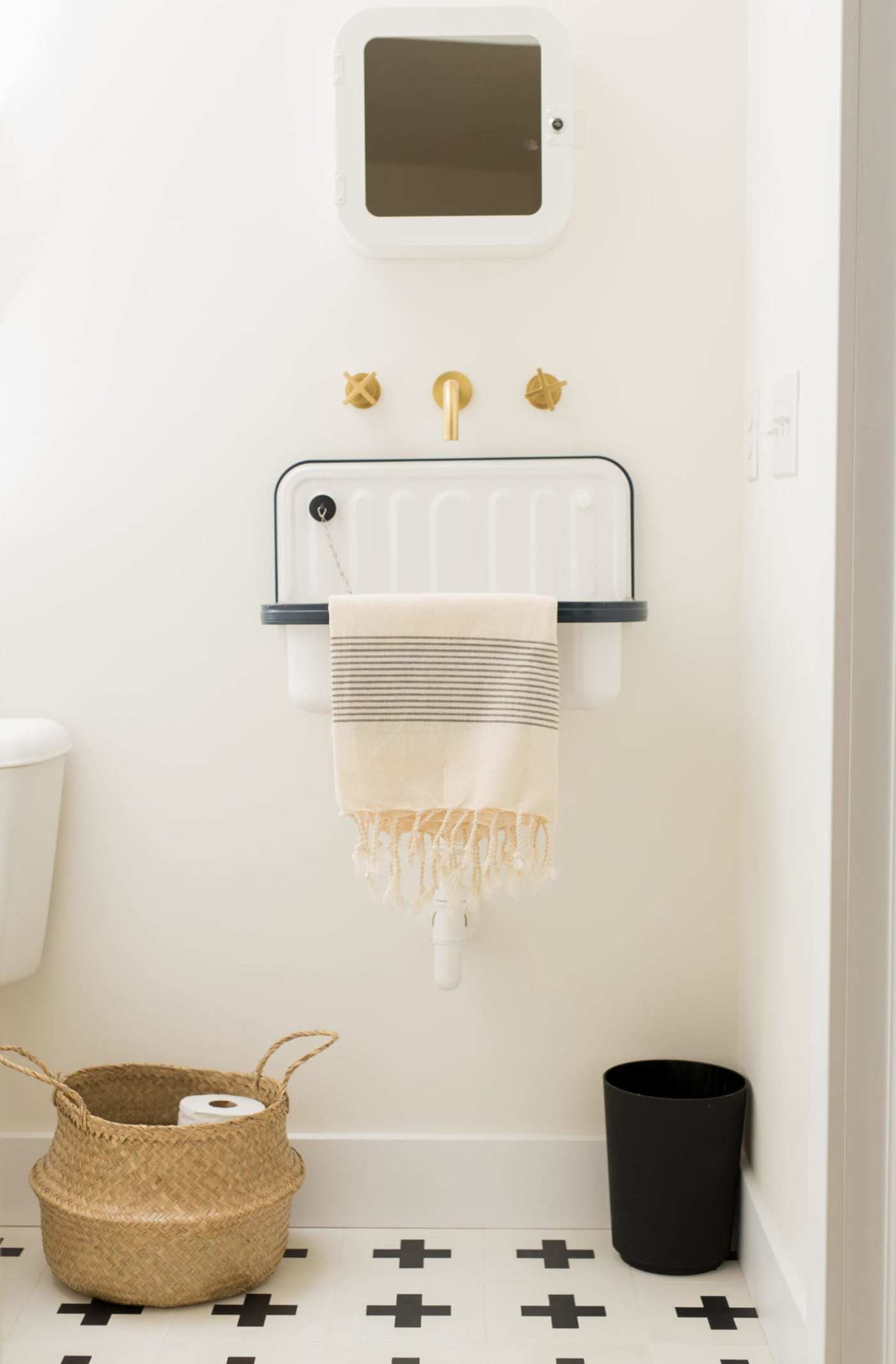 a white bathroom with black and white tile floor and a basket.