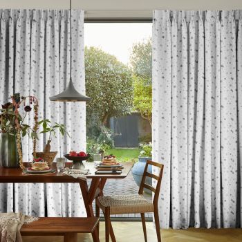 White pleated floor-length curtains with gray star pattern, parted at center to reveal a sunlit garden. They frame a dining table set for breakfast under a pendant lamp.