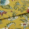 Mustard-yellow fabric with botanical green leaves and red-and-blue flowers, folded once with overlapping edge; close-up studio-lit view of the textile on a flat surface.
