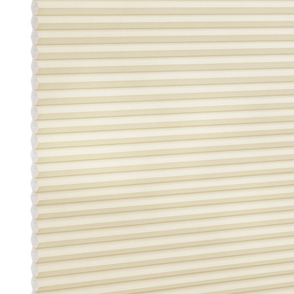 Cream-colored cellular (honeycomb) blind, fully lowered and closed, pleated horizontal cells; gently filtering diffuse light against a plain, softly lit interior with no visible window frame.