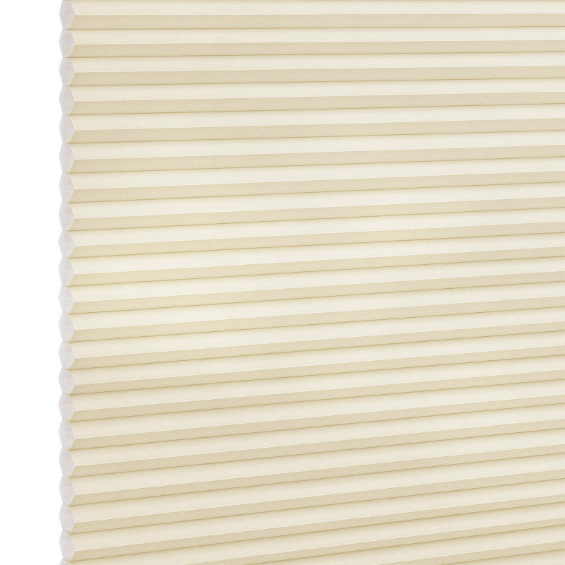 Cream-colored cellular (honeycomb) blind, fully lowered and closed, pleated horizontal cells; gently filtering diffuse light against a plain, softly lit interior with no visible window frame.