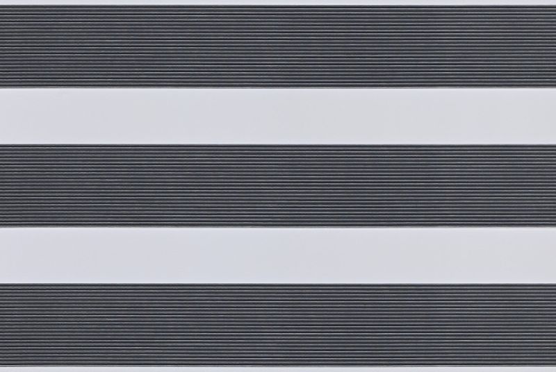 Dual-layer horizontal zebra roller blind mounted across the frame, aligned into alternating wide opaque white bands and narrow ribbed dark-gray slats, partially filtering light; interior close-up with soft even lighting.