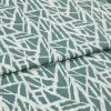 Folded teal-and-white fabric with angular abstract geometric print, folded across the center, showing overlapping layers and ribbed weave; close-up on a flat surface under soft, even lighting.
