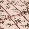 Folded fabric sample in blush pink background with linear print of bamboo shoots and leaves.