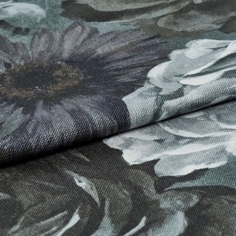 Dark floral upholstery fabric folded across the frame, coarse woven texture and oversized gray-white flower prints visible; fabric layered on itself under soft, even lighting in a close-up studio-style view.