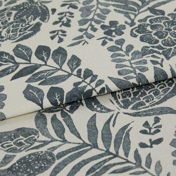 A folded cream textile with dark blue-gray botanical block-print; fabric overlapping to reveal repeated leaves and flowers; close-up studio view with soft, even lighting highlighting weave texture.