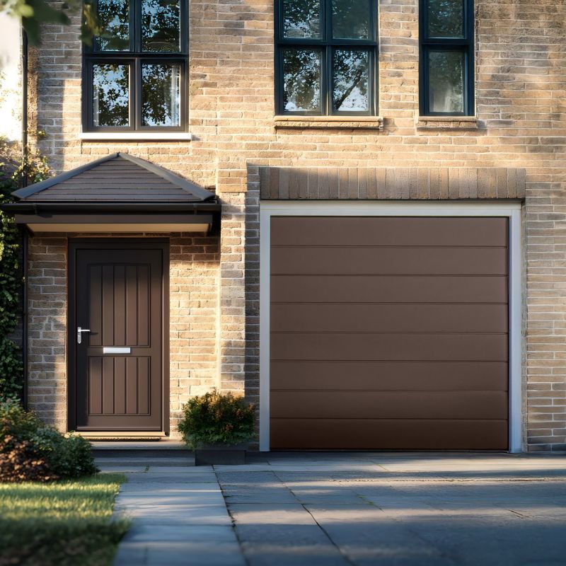 Brown horizontal-panel garage door, closed and flush in a white frame; nearby covered entry door and upper black-framed windows reflect trees, sunlit brick façade and a tidy suburban driveway.