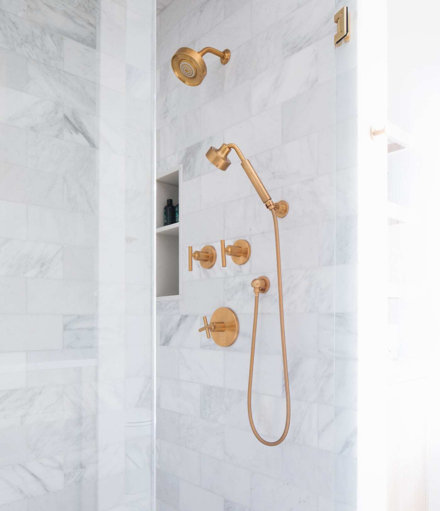 a marble tiled shower with a gold shower head.